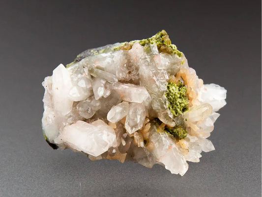 Mineral sample with green and white crystals on a gray background, branded 'Adamantine Minerals'.