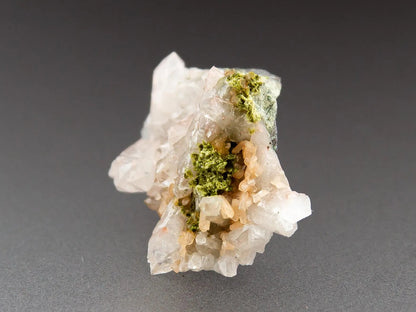 Small cluster of green epidote with microcline, surrounded by milky quartz on a gray background.