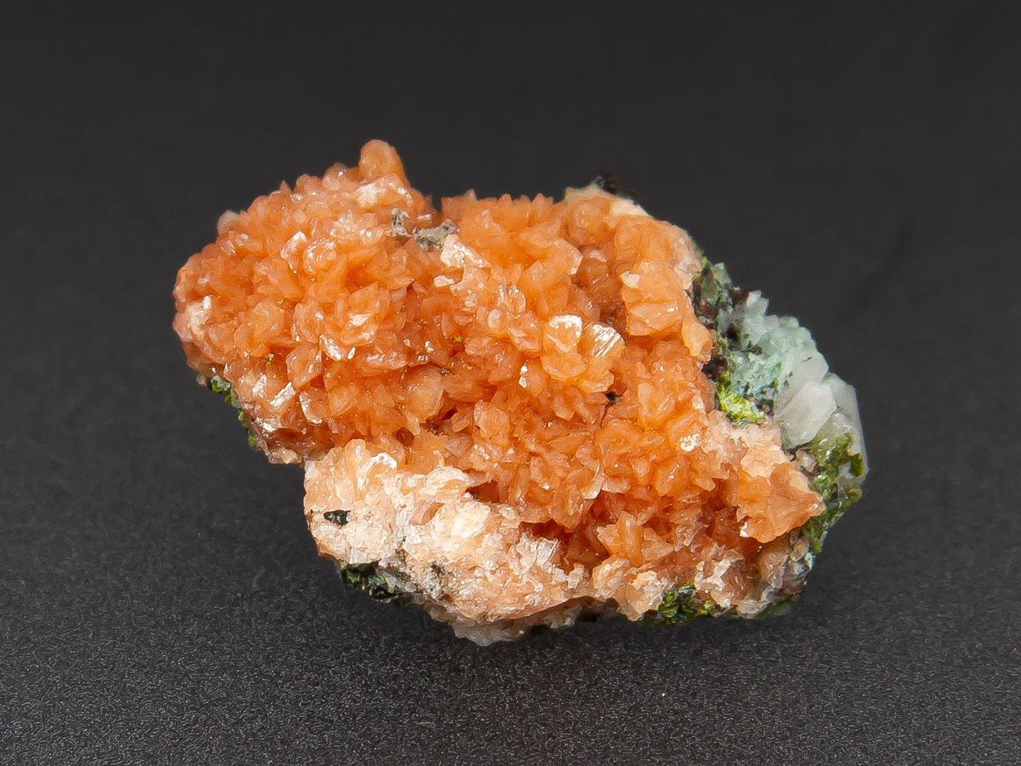 A small, orange-colored adularia crystal specimen on a dark background, with the text 'ADAMANTE MINERALS' visible.
