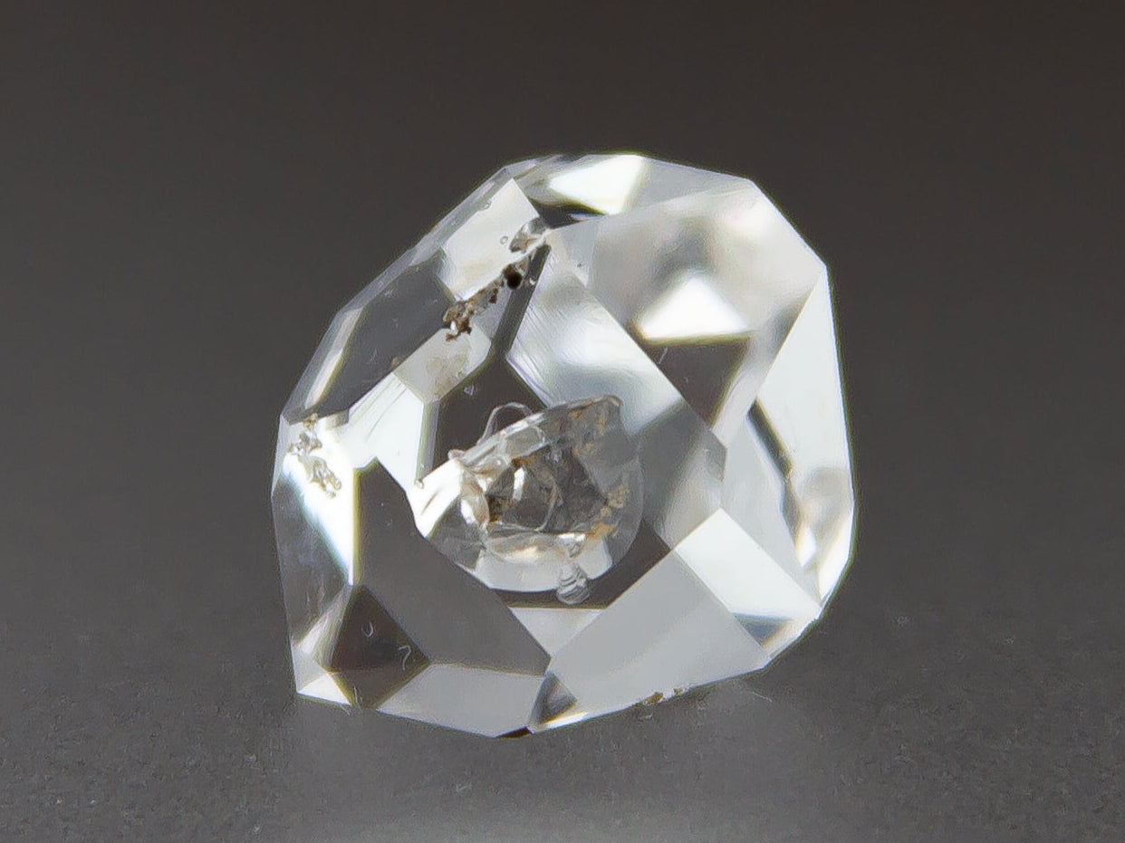 Clear crystal gemstone on a dark background with 'Adamantine Minerals' branding.