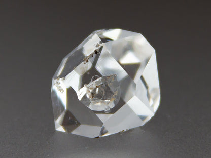 Clear crystal gemstone on a dark background with 'Adamantine Minerals' branding.