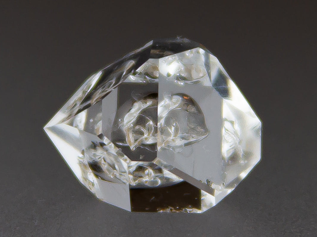 Clear crystal geometric shape on a dark background with 'Adamantine Minerals' branding.