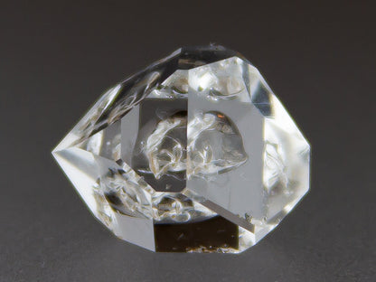 Clear crystal geometric shape on a dark background with 'Adamantine Minerals' branding.