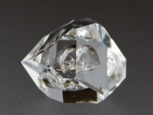 Clear crystal geometric shape on a dark background with 'Adamantine Minerals' branding.