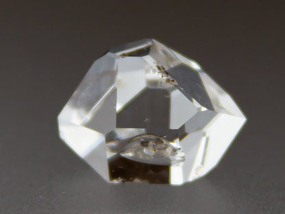 Clear crystal with geometric facets on a dark background, branded 'Adamantine Minerals'.