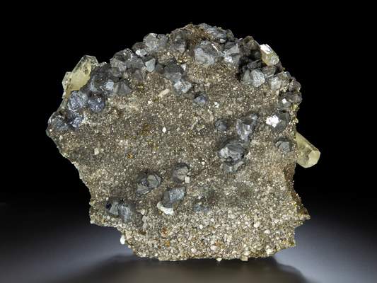 Cubic galena crystals on a large piece of matrix with tiny sand-sized chalcopyrite crystals and dolomite. Several semi-transparent calcite columns protrude from the sides of the specimen.