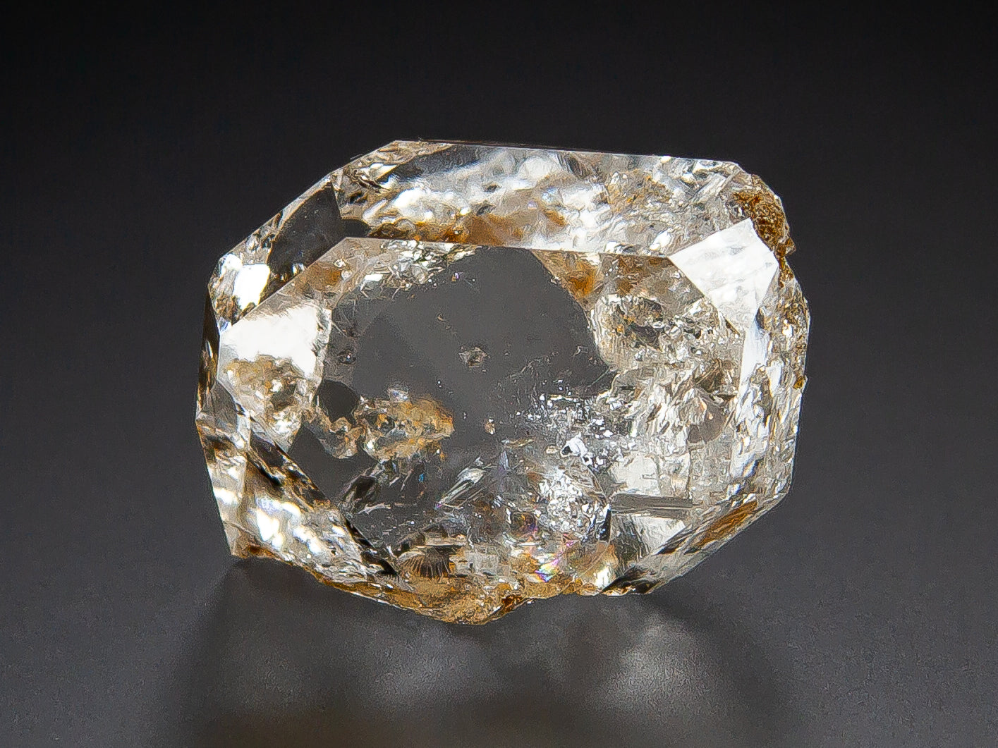 Herkimer Diamond with natural inclusions and brownish mineral deposits, photographed on a dark gray to black background.
