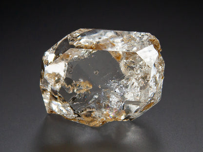 Herkimer Diamond with natural inclusions and brownish mineral deposits, photographed on a dark gray to black background.