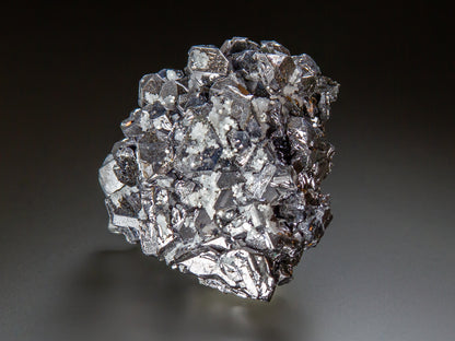 A metallic silver galena cluster with sharp, reflective facets, photographed on a dark-to-light gray gradient studio background.