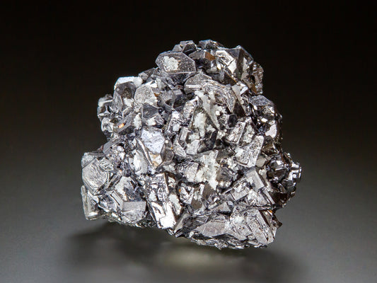 A metallic silver crystal cluster of galena, photographed on a dark gray to black gradient background.
