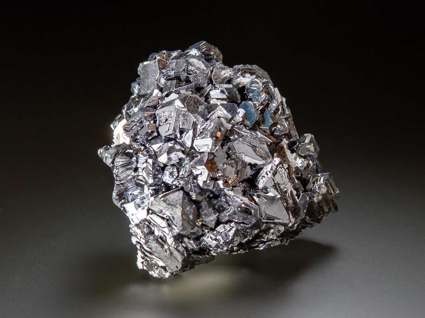 A metallic silver crystal cluster with sharp, reflective facets, photographed on a dark gradient studio background.