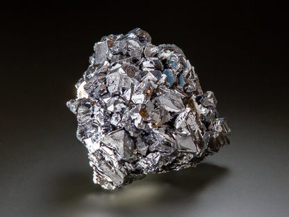A metallic silver crystal cluster with sharp, reflective facets, photographed on a dark gradient studio background.