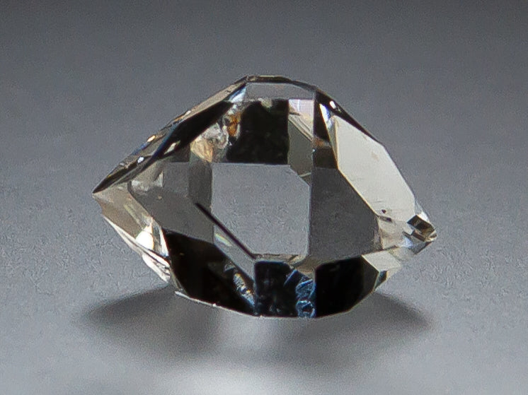 A clear Herkimer Diamond with double terminations, photographed on a smooth gray surface with a soft shadow.