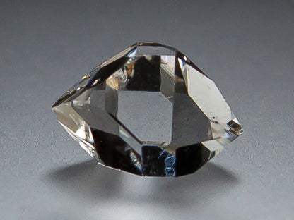 A clear Herkimer Diamond with double terminations, photographed on a smooth gray surface with a soft shadow.