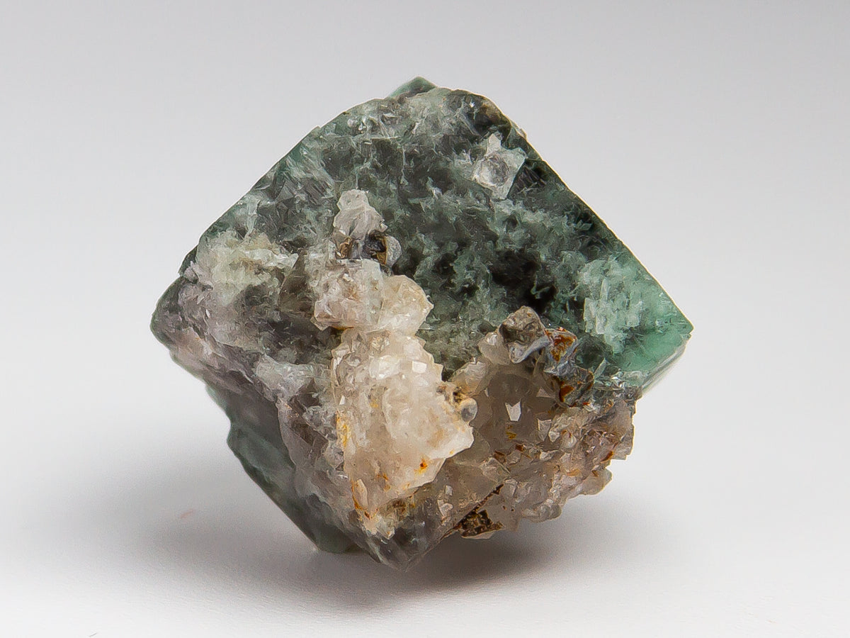 A raw mineral specimen featuring a greenish-gray matrix with prominent white and translucent crystal clusters, photographed on a neutral light gray background.