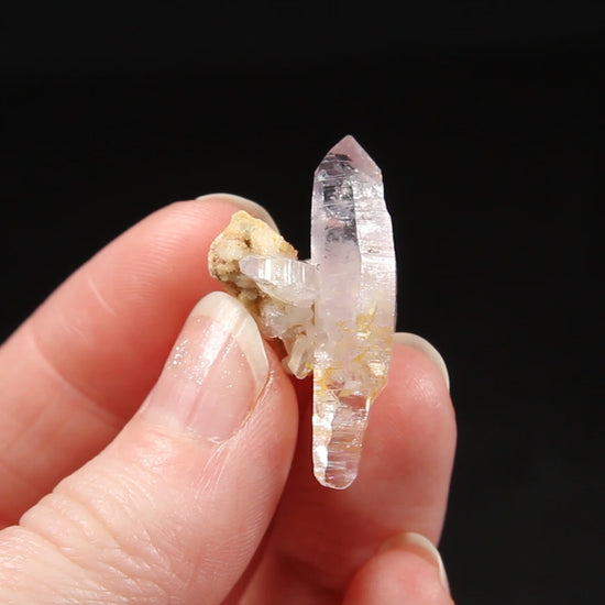 A glistening quartz crystal with slight purple color near terminations. Striations are present on parallel faces as well as stepped crystal growth.